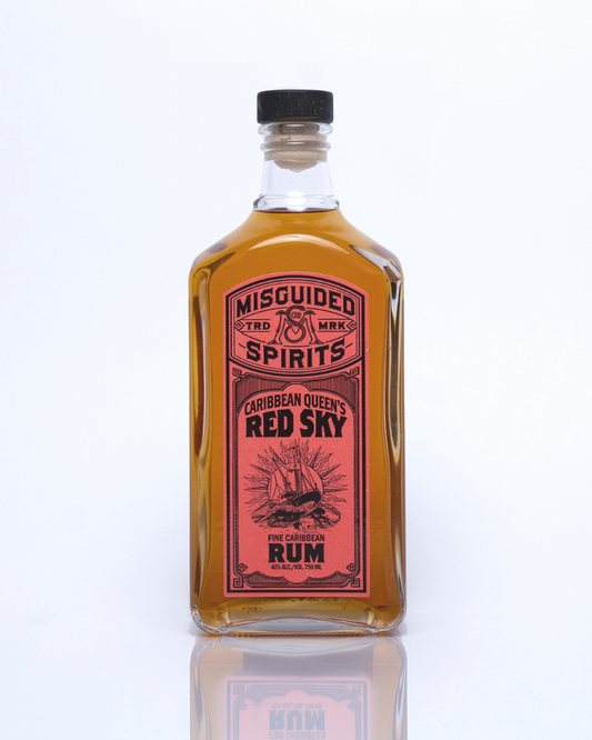750ml bottle of Misguided Spirits Caribbean Queen's Red Sky Aged Rum with a red label and a rum runner ship on the label. The rum is a rich warm caramel color. 